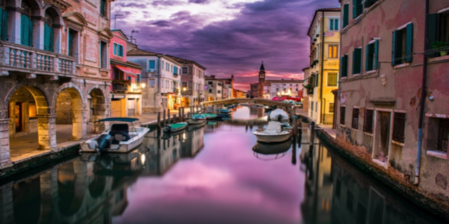 Venice's canals dance with sunset hues as a lone gondola gracefully weaves through the enchanting waterways, painting a canvas of timeless beauty.