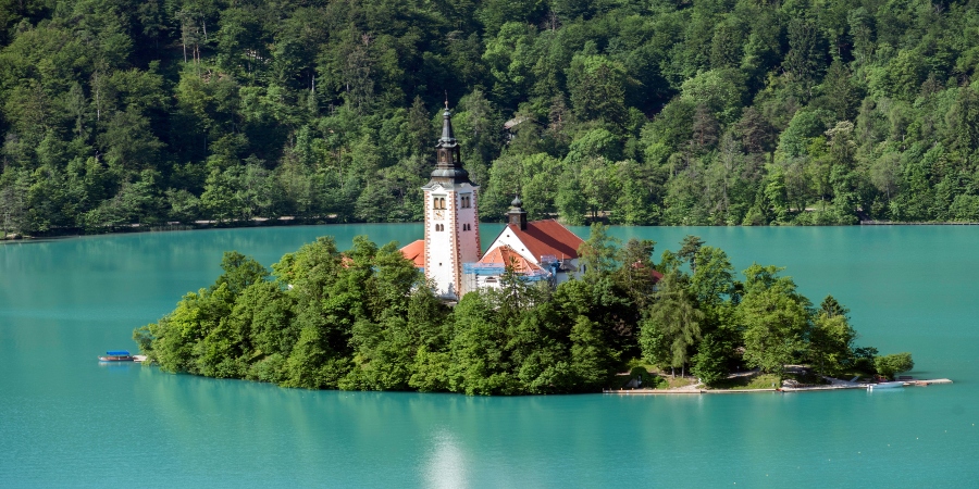 A tranquil view of Lake Bled surrounded by lush greenery and the Julian Alps - a hidden gem in Europe's summer landscape